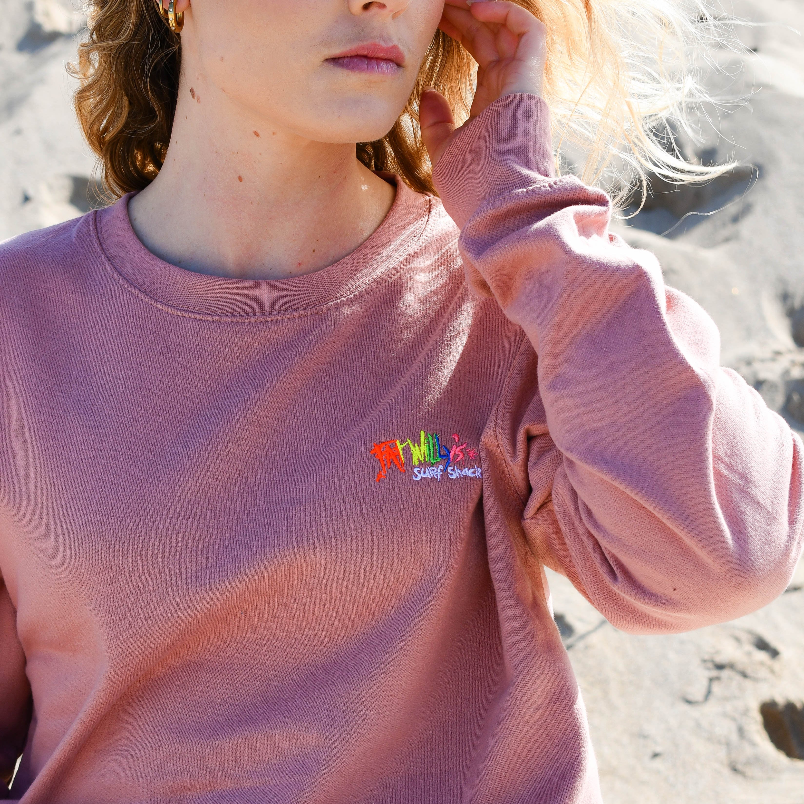 Person wearing a pink sweatshirt with a colorful logo on a beach