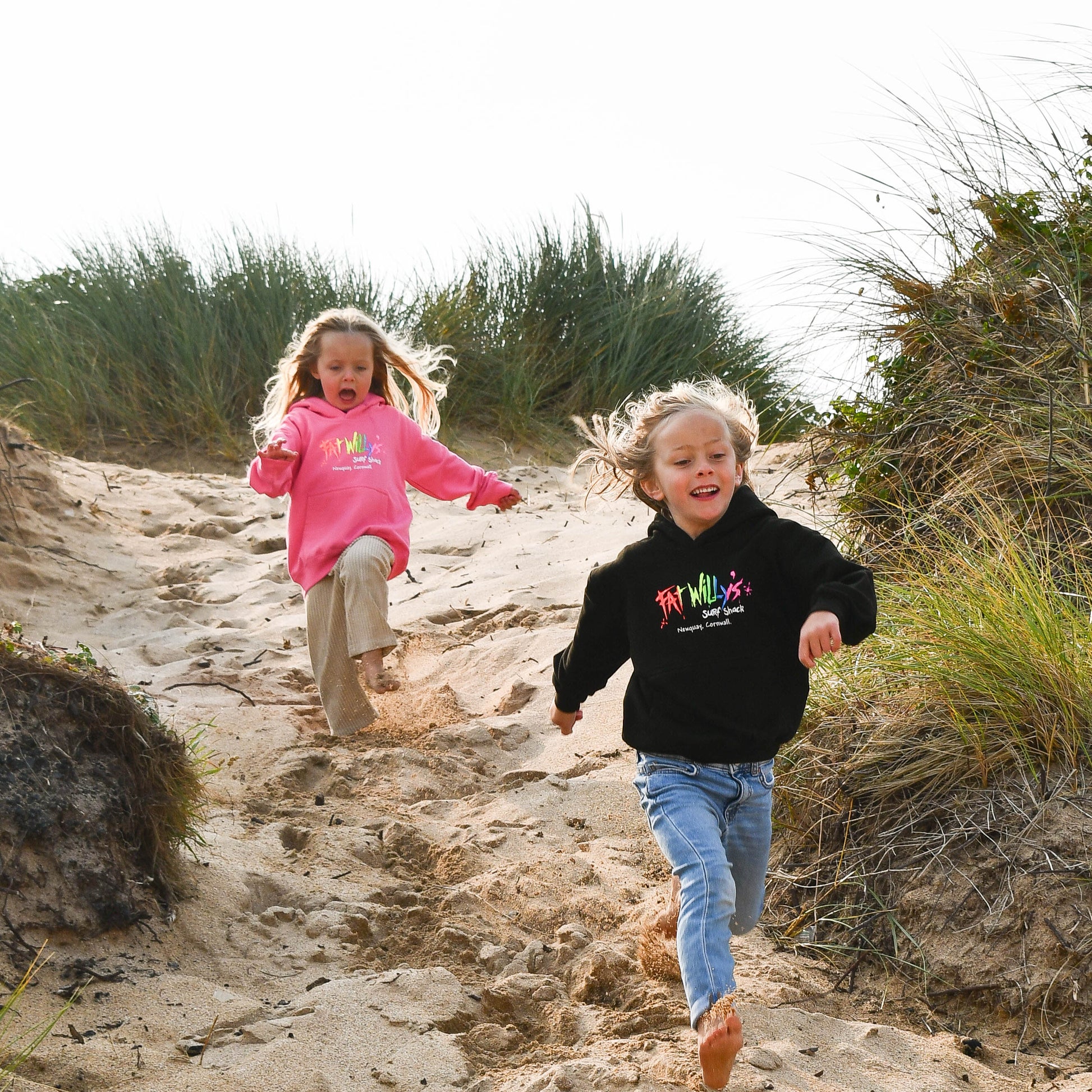 Two children running up a sandy dune with grasses in the background