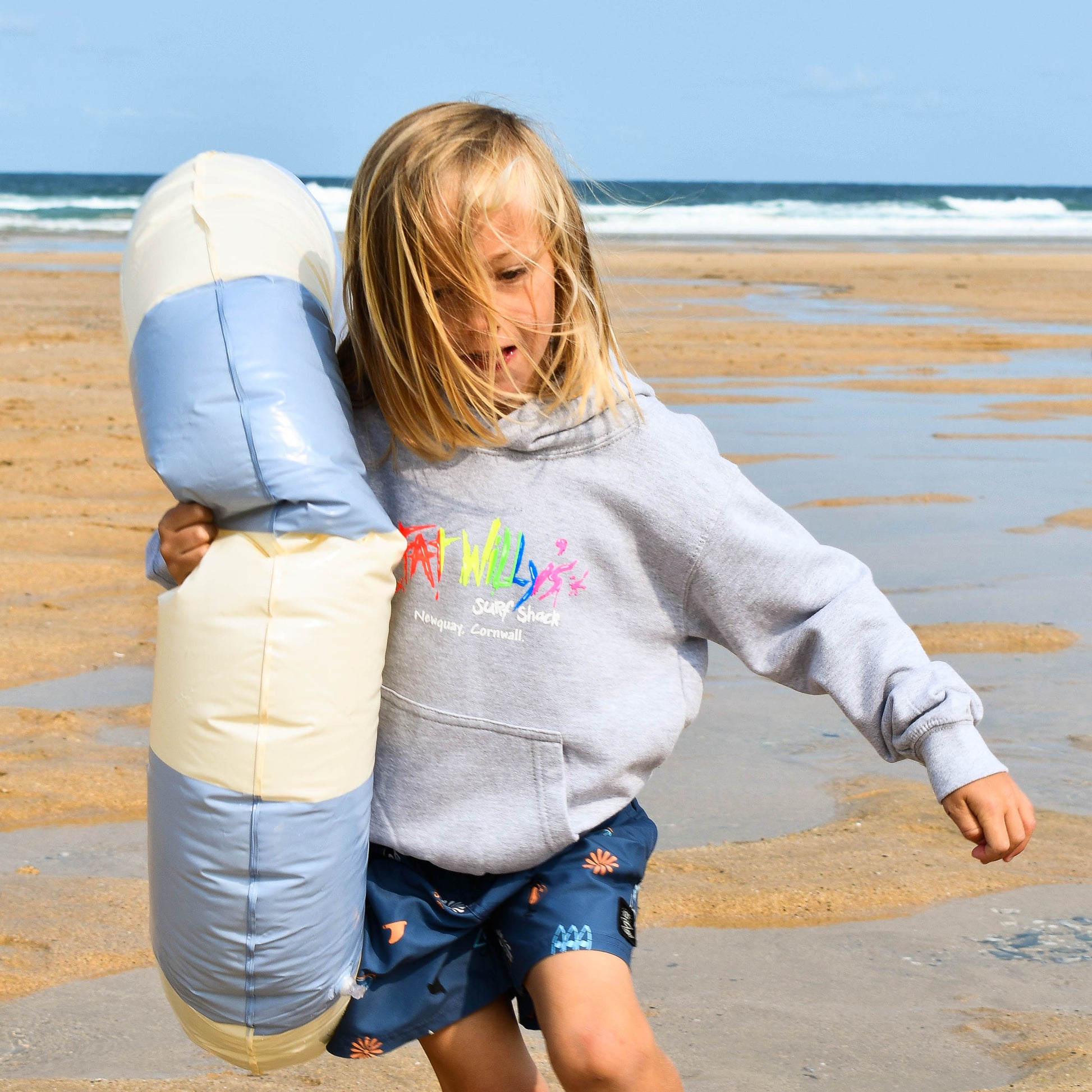 Child holding a large plush toy on a beach with ocean waves in the background