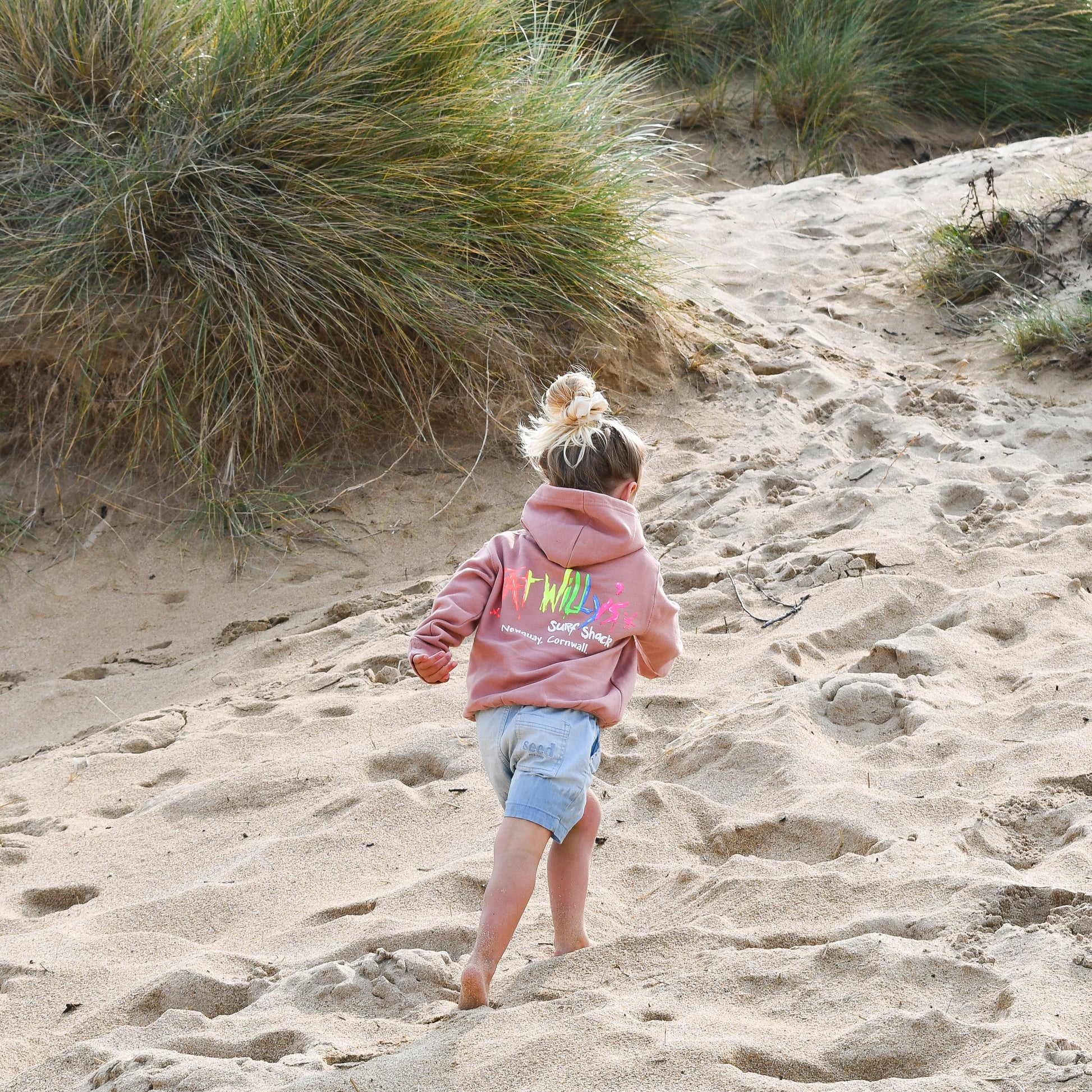 Child walking on a sandy path with grasses in the background