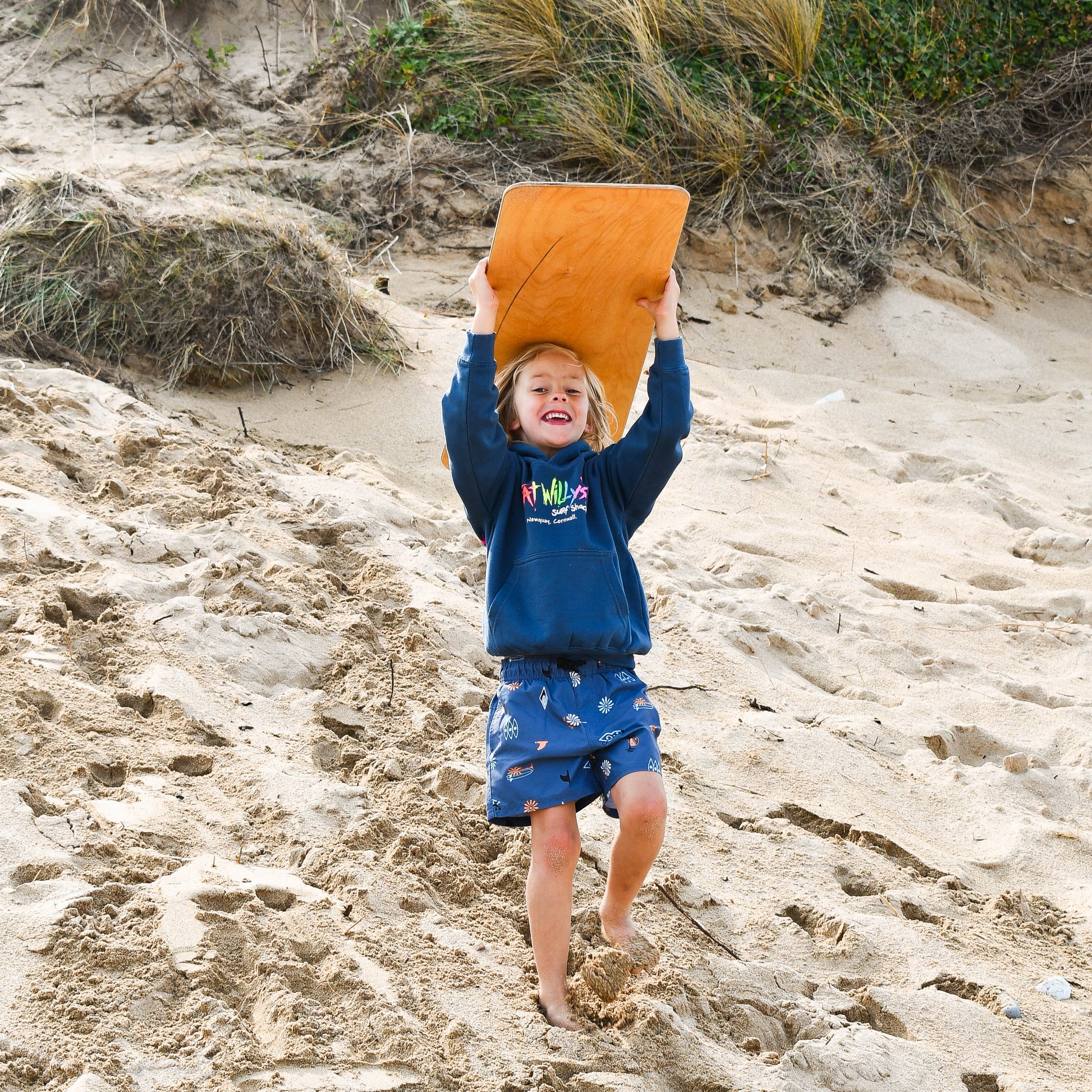 Child playing on a sandy beach with an orange sandcastle mold.