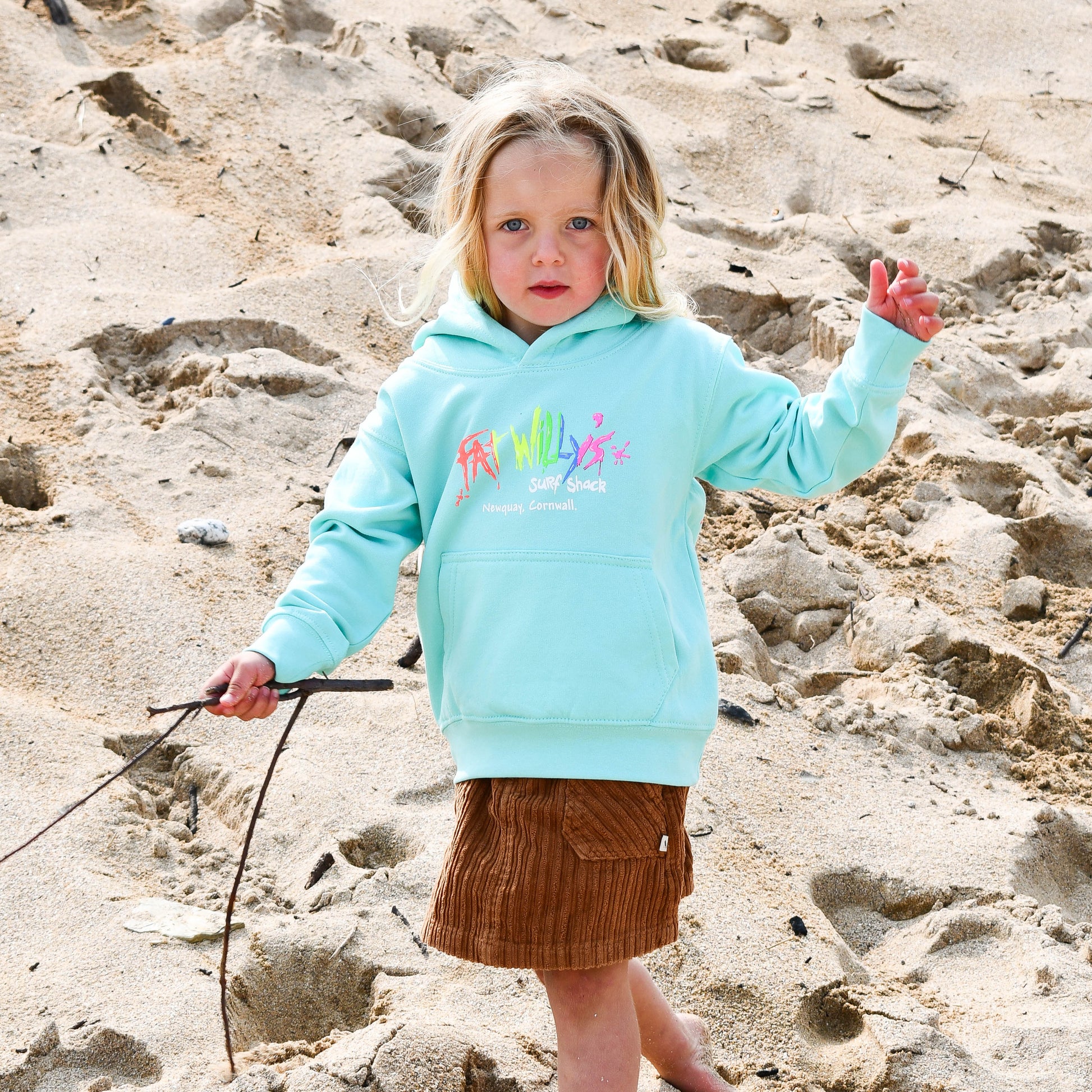 Child wearing a light blue hoodie with colorful text on a sandy beach