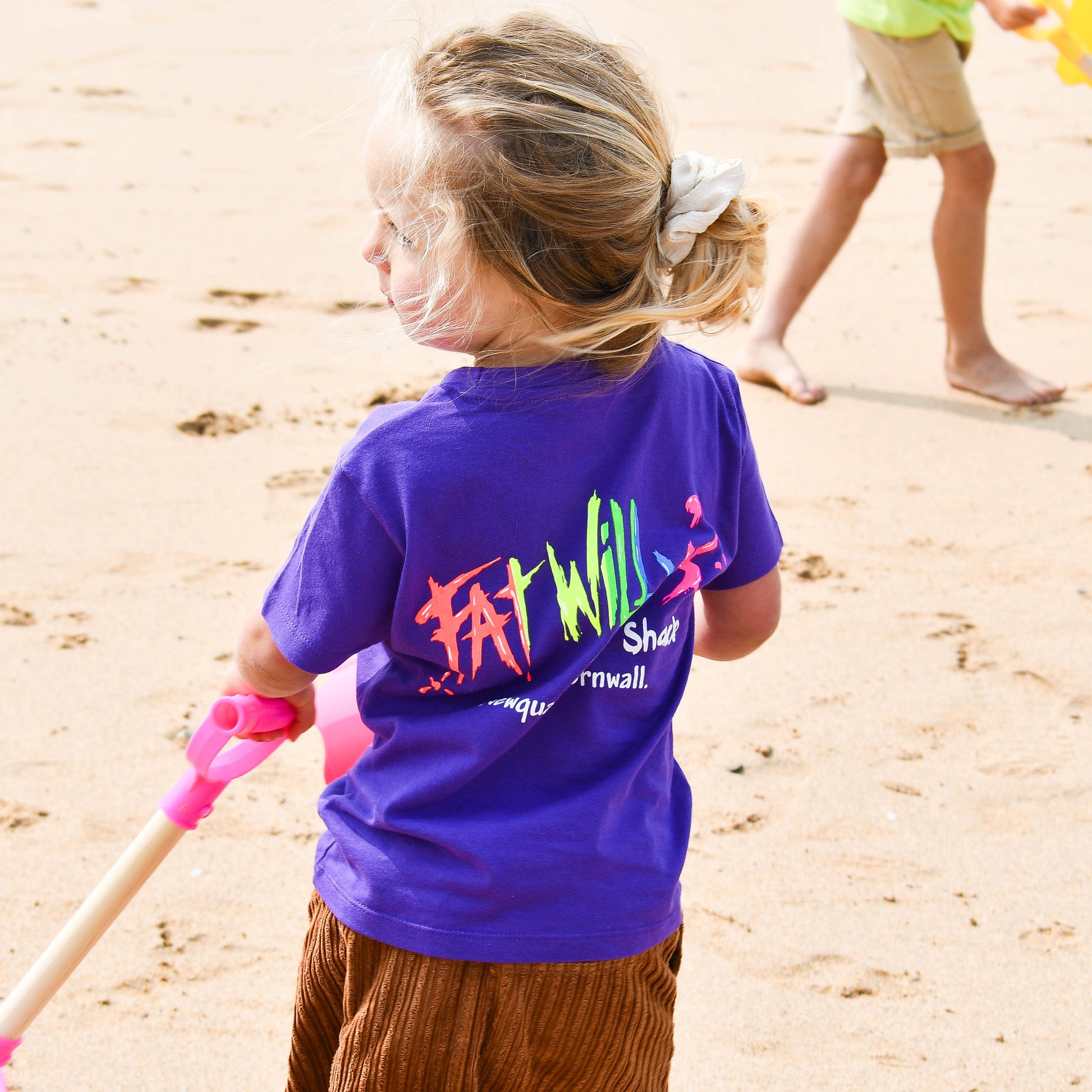Child wearing a purple shirt with colorful text on a sandy beach
