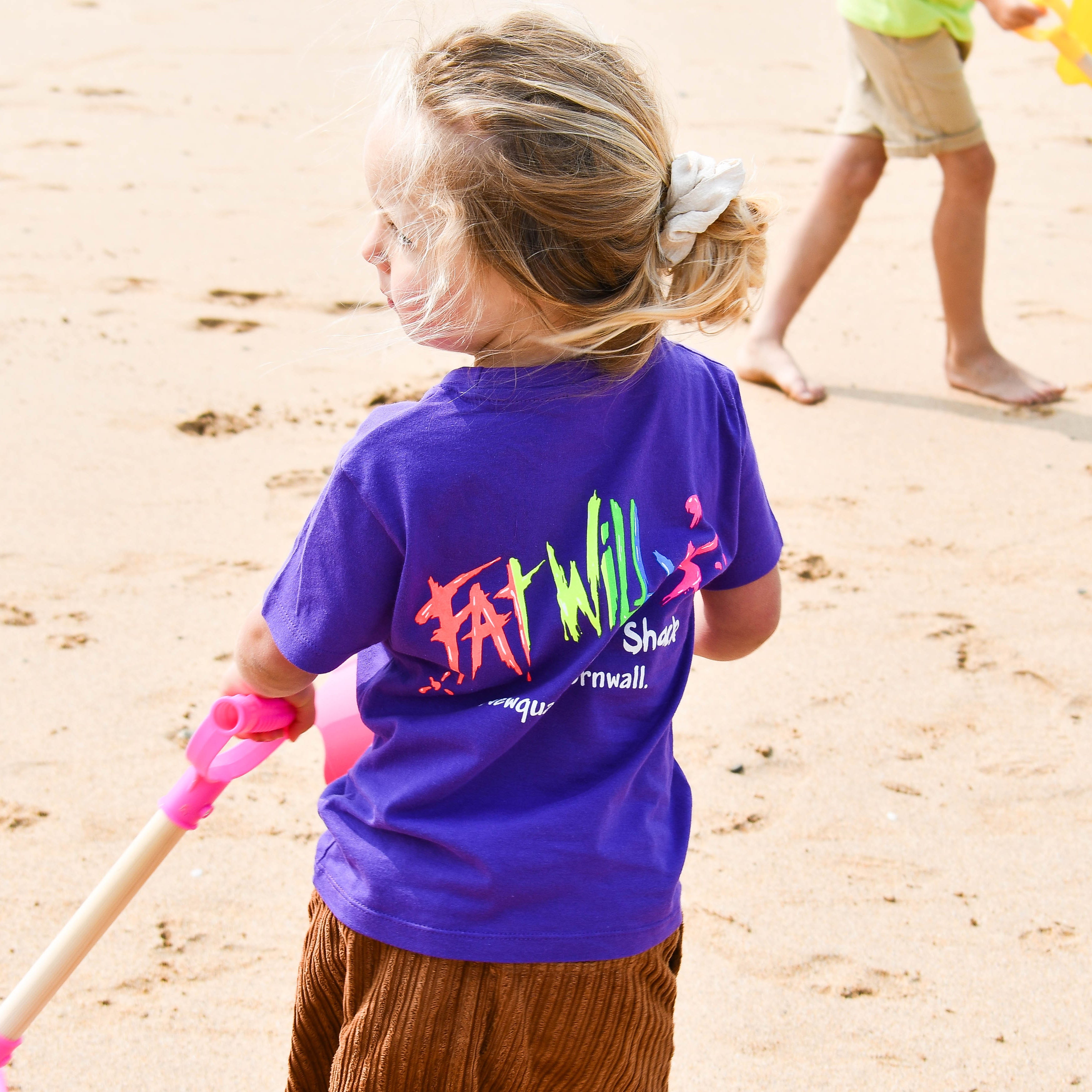 Child wearing a purple shirt with colorful text on a sandy beach