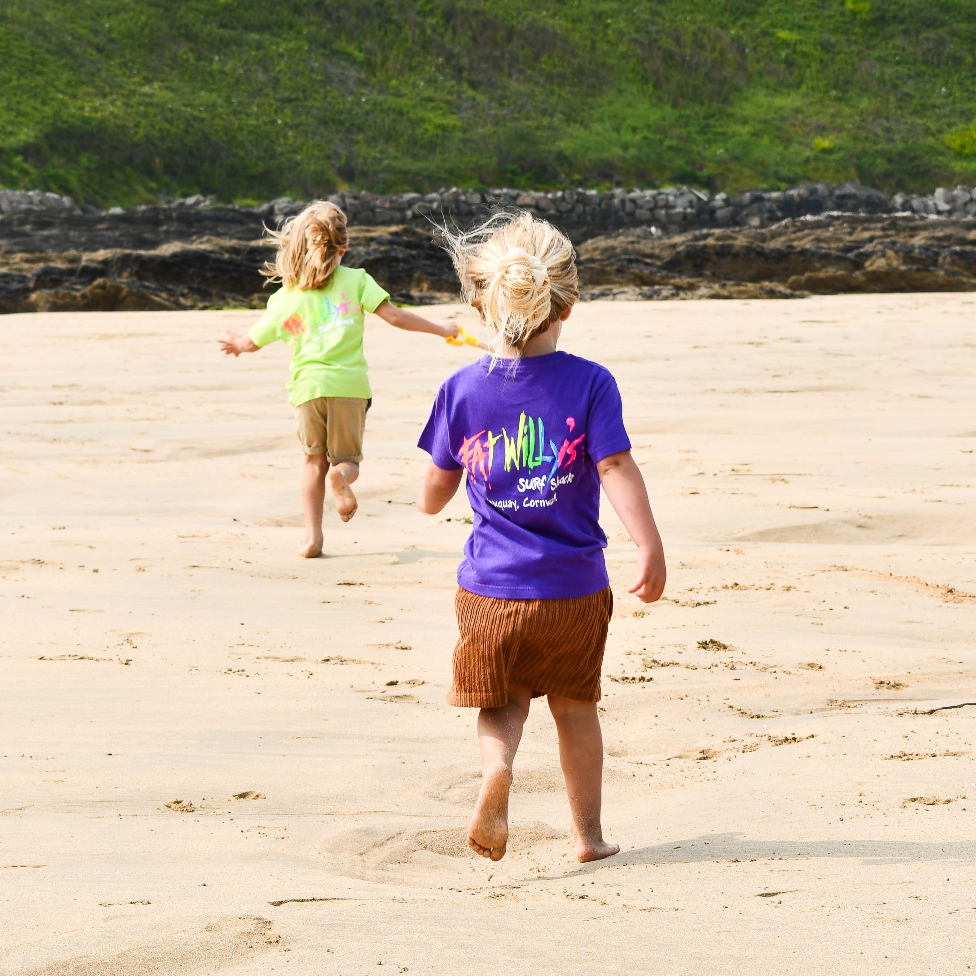 Two children running on a sandy beach with buildings in the background