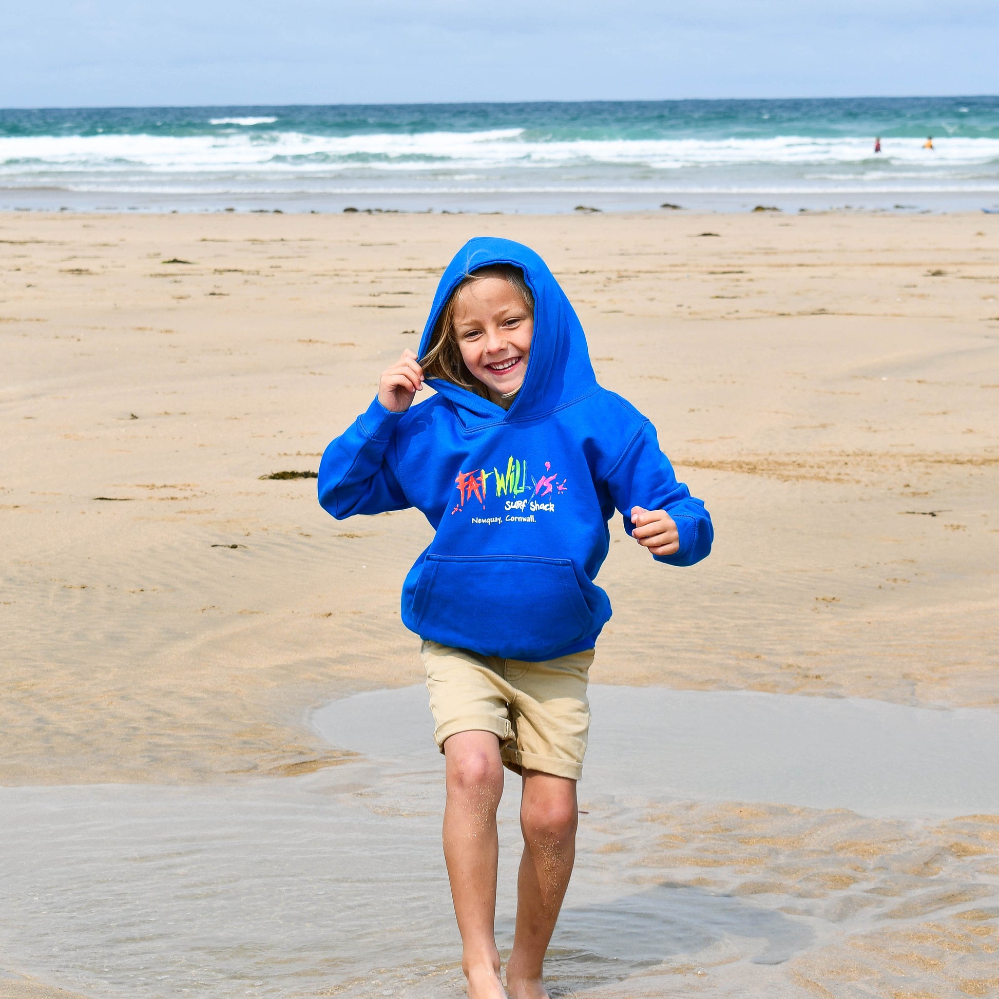 Child in a blue hoodie running on a sandy beach with ocean waves in the background