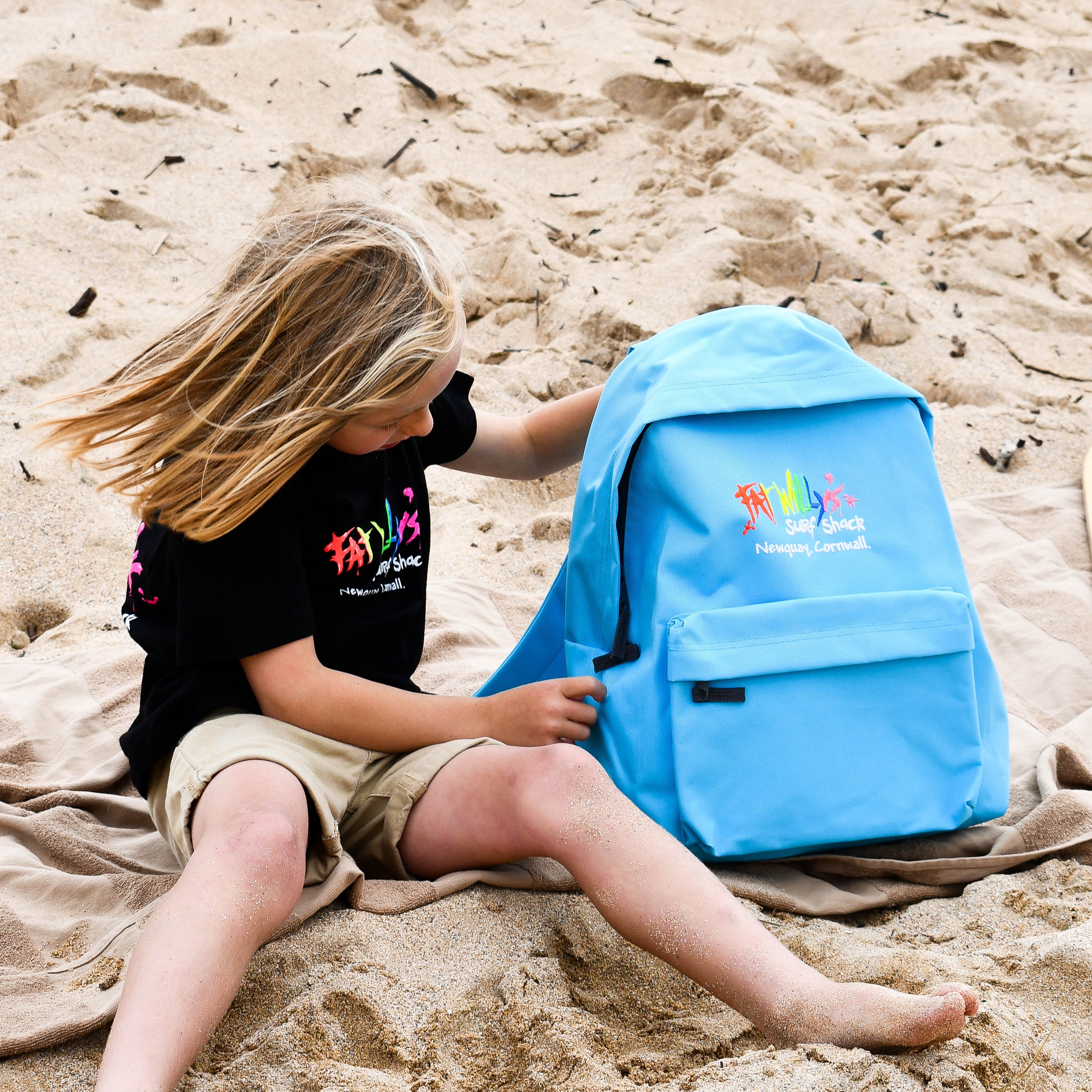 Child sitting on sand with a blue backpack