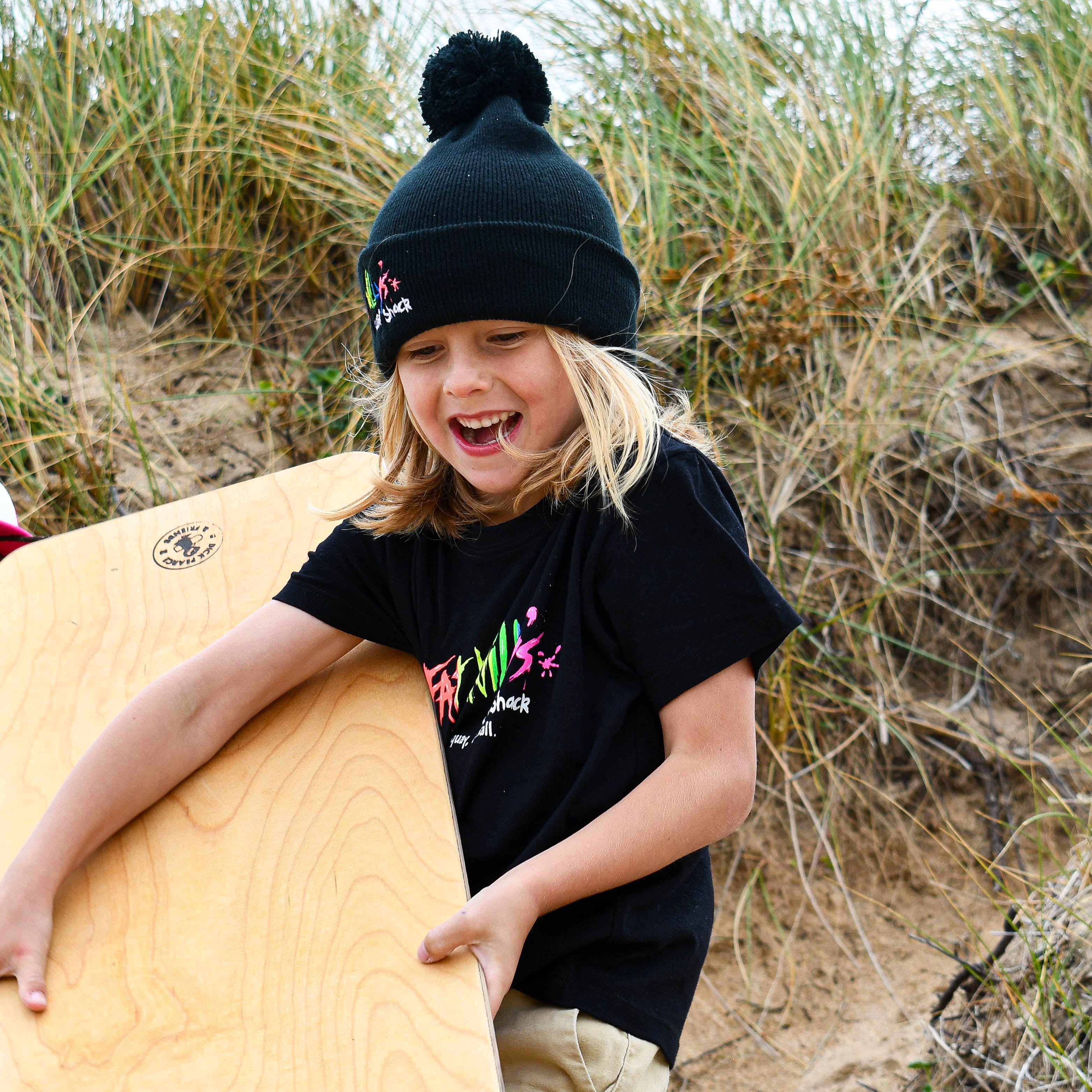 Child holding a surfboard on a beach with grass and sand in the background