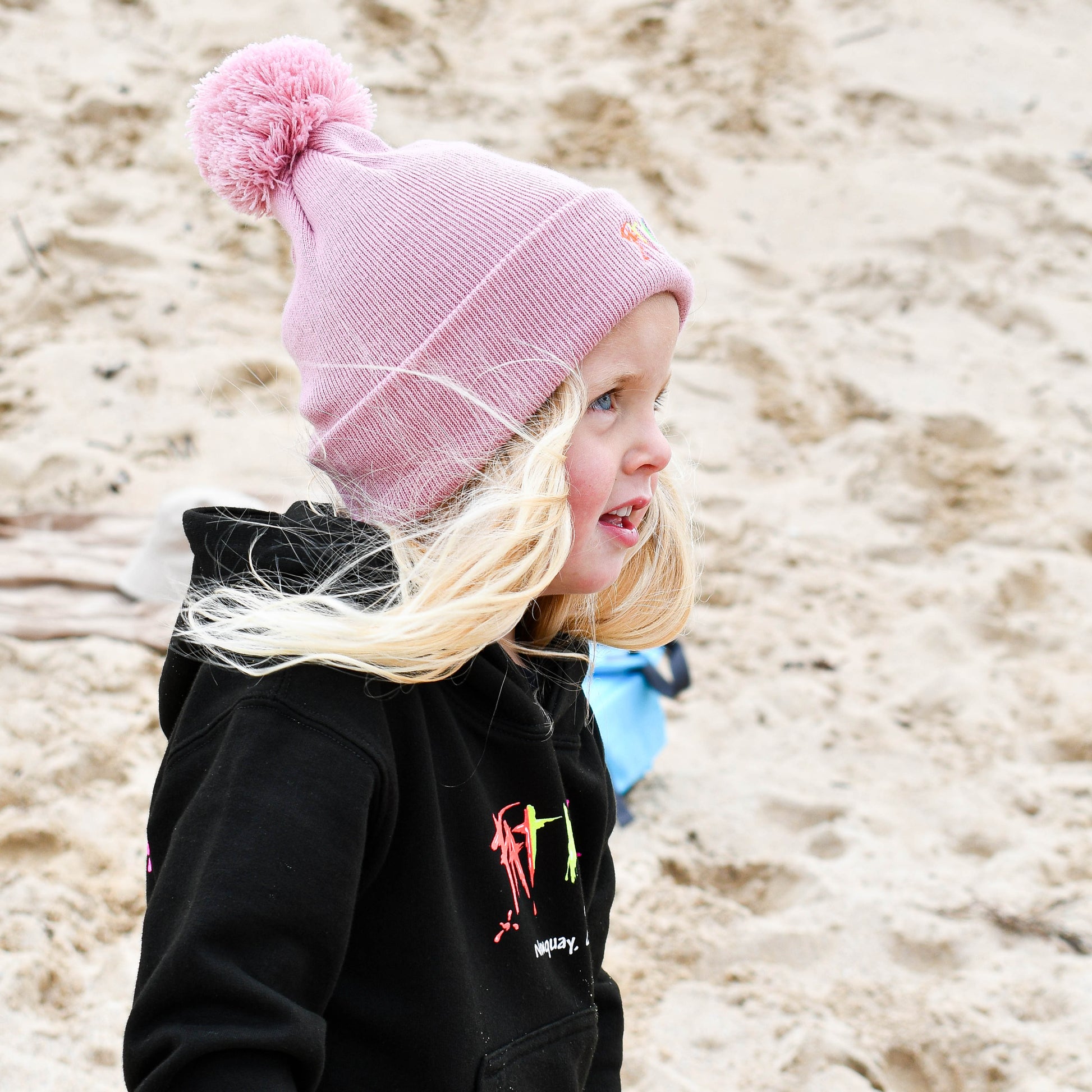 Child wearing a pink beanie and black jacket on a sandy beach