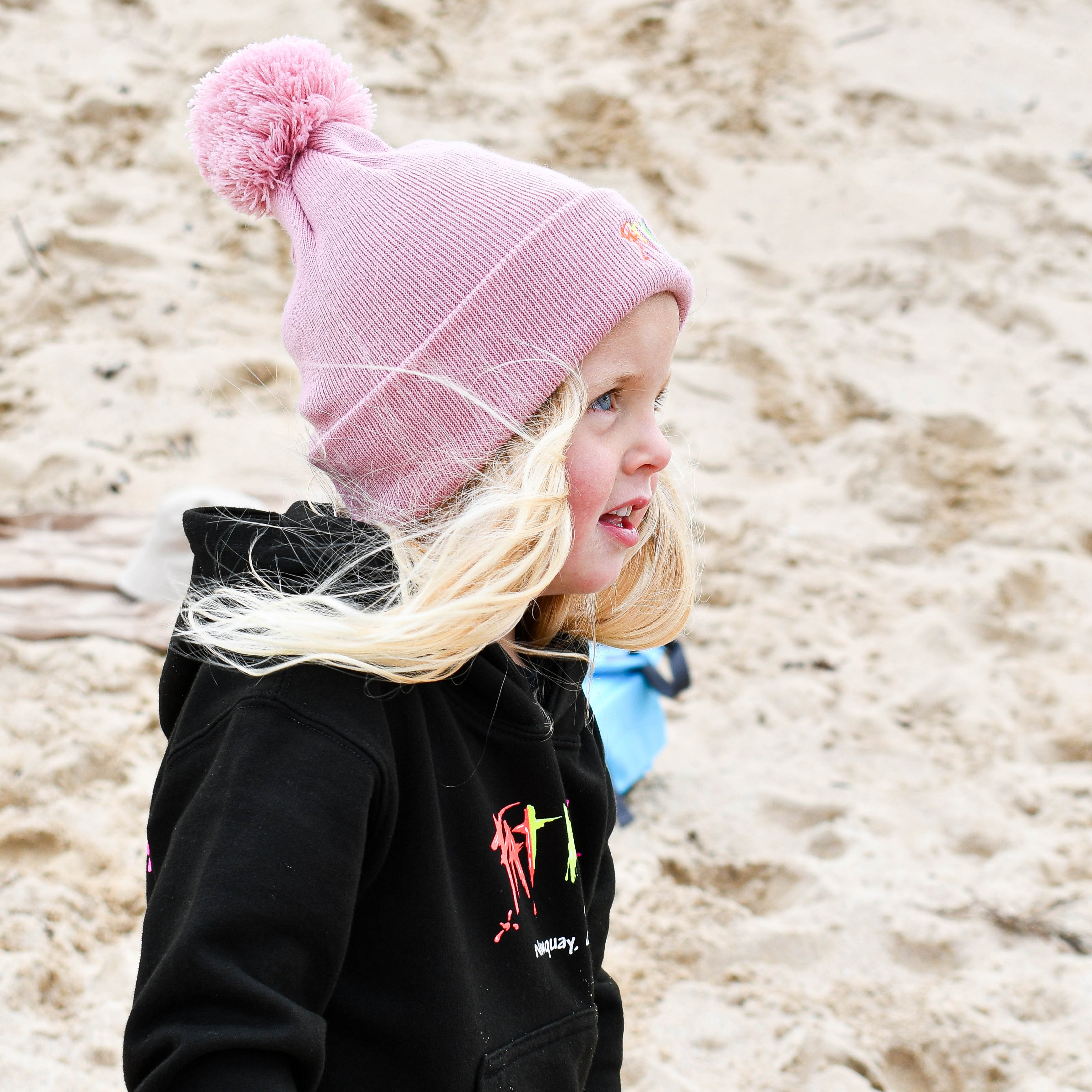 Child wearing a pink beanie and black jacket on a sandy beach