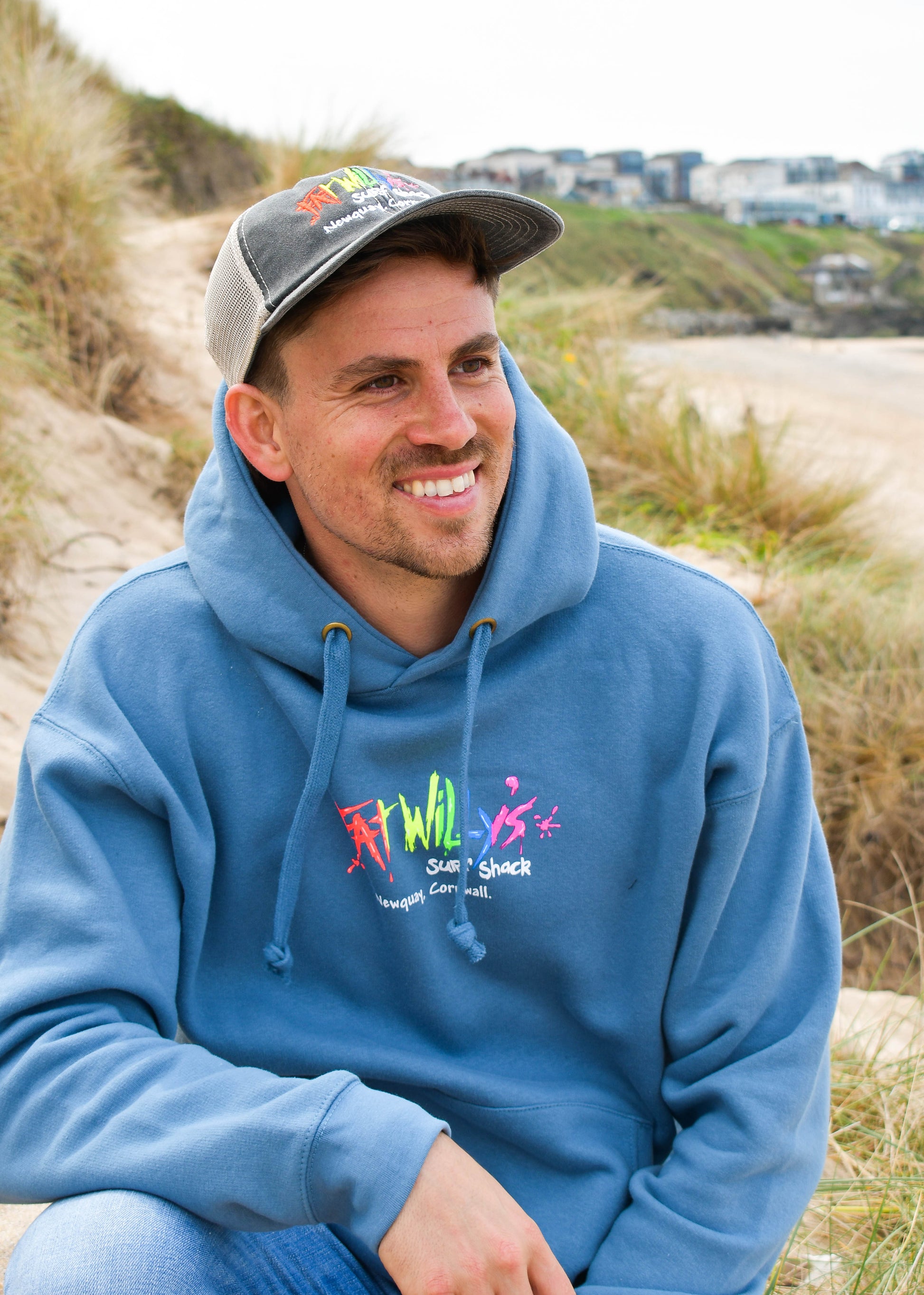 Man wearing a blue hoodie with colorful graphics and text, sitting outdoors.